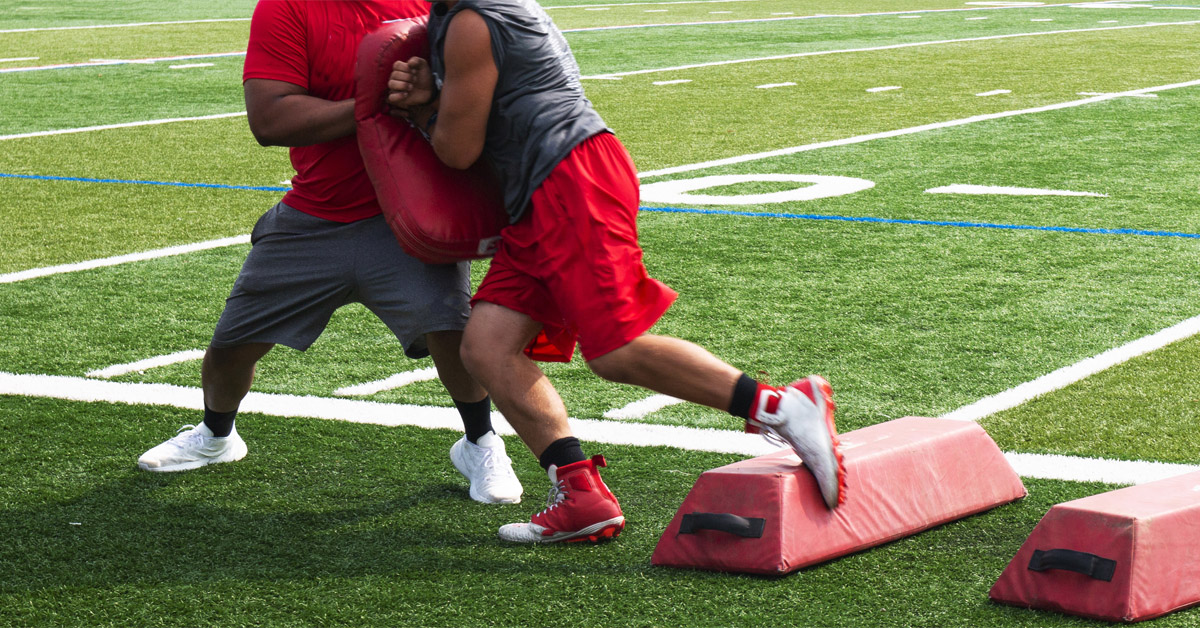 Football player practicing shoulder block with coach